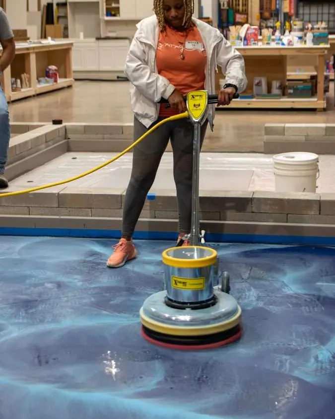 A student runs a floor machine across a blue metallic epoxy floor in the training bay