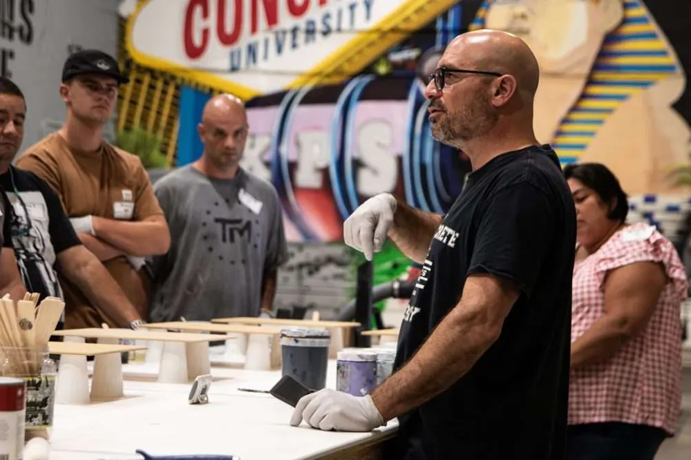 An instructor explains a technique to a small group of students at a work table